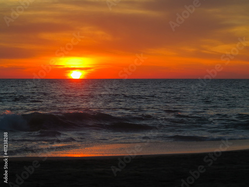 A beautiful red and orange sunset over the Pacific Ocean the silhouettes of beachgoers outlined against the water of Puerto Escondito  Mexico.  Image has copy space.