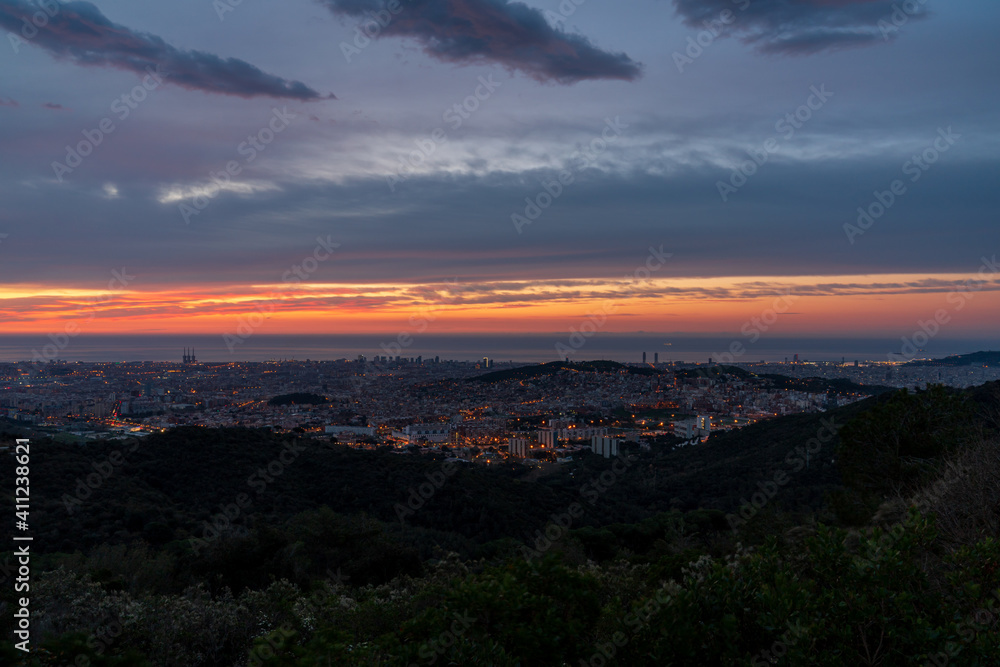 Sunrise on a spring day in the city of Barcelona. We can see the sky, with some clouds that light up like fire, with the sunlight. The water of the Mediterranean Sea, completely flat.