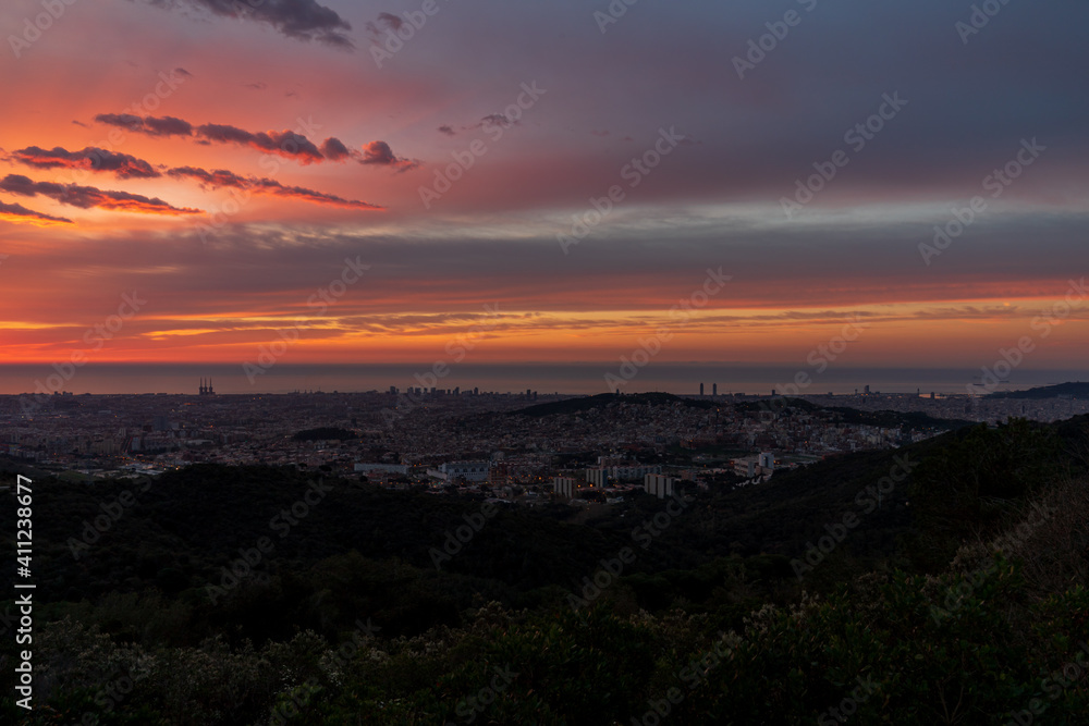 Sunrise on a spring day in the city of Barcelona. We can see the sky, with some clouds that light up like fire, with the sunlight. The water of the Mediterranean Sea, completely flat.