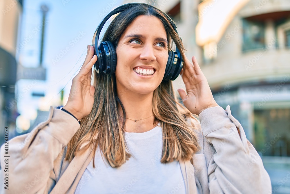 Young caucasian woman smiling happy listening to music using headphones at the city.