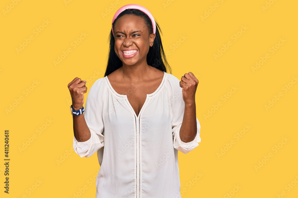 Young black woman wearing casual clothes excited for success with arms raised and eyes closed celebrating victory smiling. winner concept. Young black woman wearing casual clothes excited for success with arms raised and eyes closed celebrating victory smiling. winner concept.