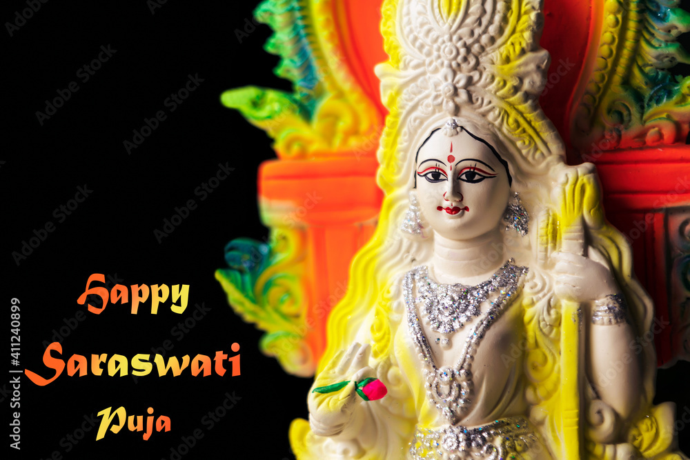 Fototapeta premium Happy Basant Panchami. Happy Saraswati Puja Background. Colorful clay idol of Goddess Swaraswati holding a veena, isolated in black on Vasant Panchami. Hindu religious festival, culture, tradition