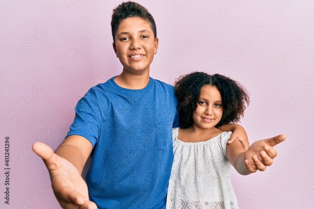 Young hispanic family of brother and sister wearing casual clothes together smiling cheerful offering palm hand giving assistance and acceptance. Young hispanic family of brother and sister wearing casual clothes together smiling cheerful offering palm hand giving assistance and acceptance.