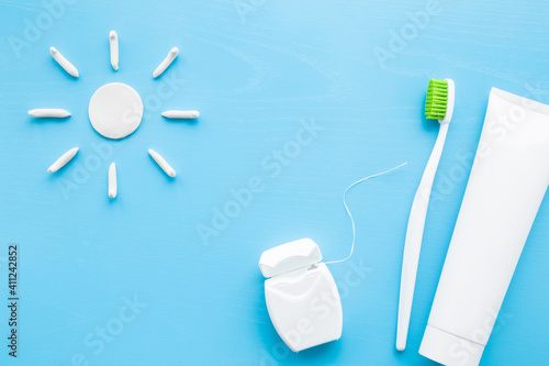 Toothbrush with green bristles, white tube of toothpaste, dental floss on light blue table background. pastel color. Sun created from paste. Healthy teeth. Morning routine. Top down view. Closeup.