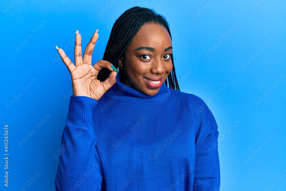 Young african american woman wearing casual winter sweater smiling positive doing ok sign with hand and fingers. successful expression. Young african american woman wearing casual winter sweater smiling positive doing ok sign with hand and fingers. successful expression.