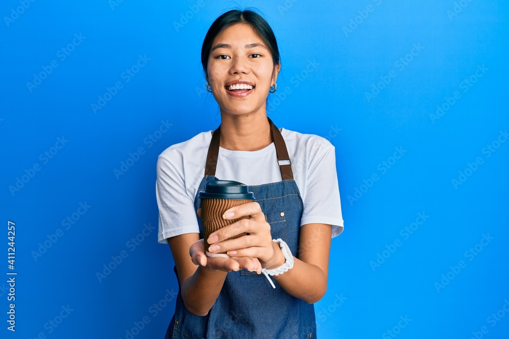 Young chinese woman wearing waiter apron holding cup of coffee smiling and laughing hard out loud because funny crazy joke. Young chinese woman wearing waiter apron holding cup of coffee smiling and laughing hard out loud because funny crazy joke.