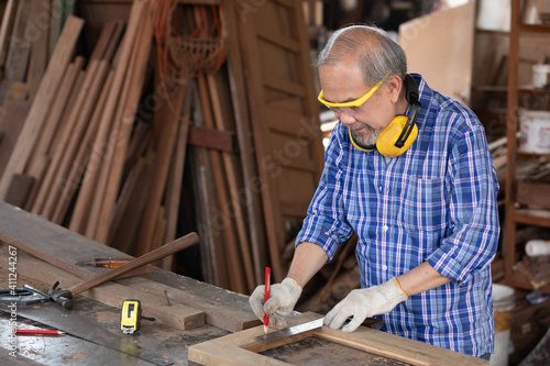 senior man carpenter measuring wood with ruler in workshop