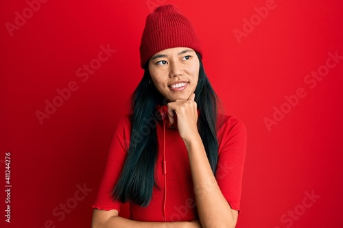 Young chinese woman listening to music using headphones with hand on chin thinking about question, pensive expression. smiling with thoughtful face. doubt concept.