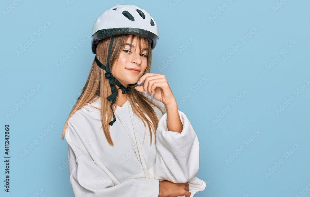 Teenager caucasian girl wearing bike helmet looking confident at the camera with smile with crossed arms and hand raised on chin. thinking positive. Teenager caucasian girl wearing bike helmet looking confident at the camera with smile with crossed arms and hand raised on chin. thinking positive.
