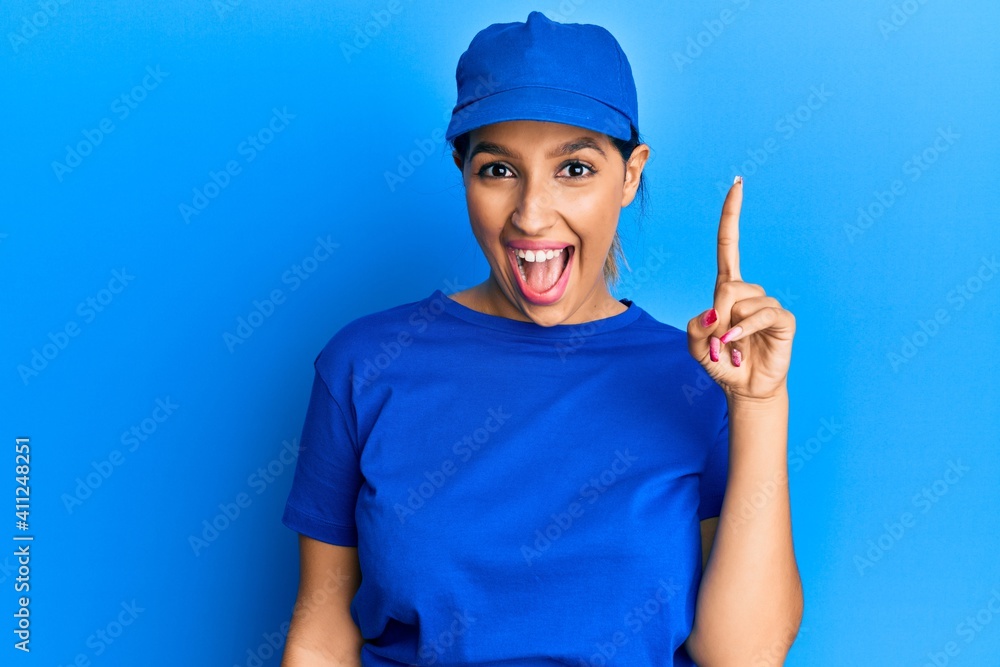 Beautiful brunette woman wearing delivery uniform pointing finger up with successful idea. exited and happy. number one.