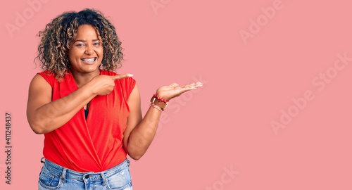 Young african american plus size woman wearing casual style with sleeveless shirt amazed and smiling to the camera while presenting with hand and pointing with finger.