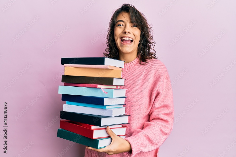 Young hispanic woman holding a pile of books smiling and laughing hard out loud because funny crazy joke. Young hispanic woman holding a pile of books smiling and laughing hard out loud because funny crazy joke.
