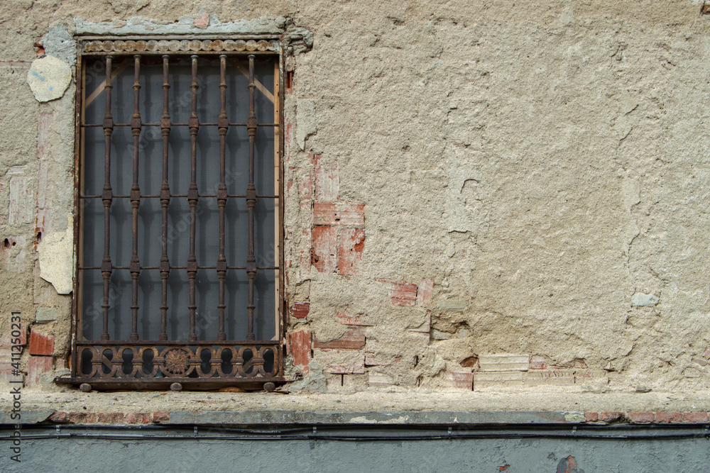 old window with grating in a peeling wall