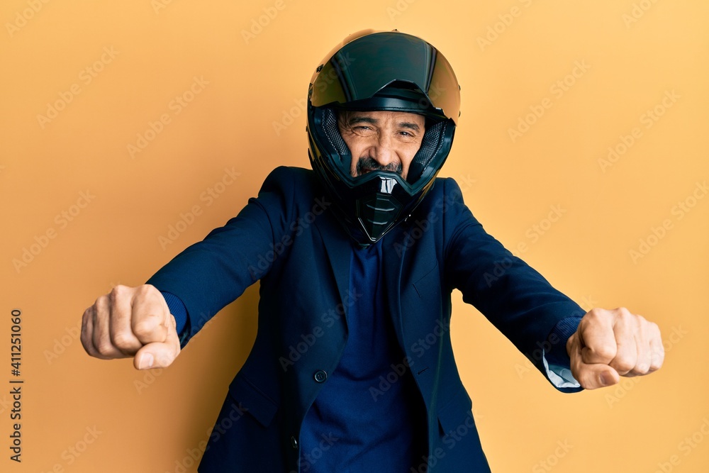 Middle age hispanic man wearing motorcycle helmet doing moto symbol with hands smiling and laughing hard out loud because funny crazy joke. Middle age hispanic man wearing motorcycle helmet doing moto symbol with hands smiling and laughing hard out loud because funny crazy joke.