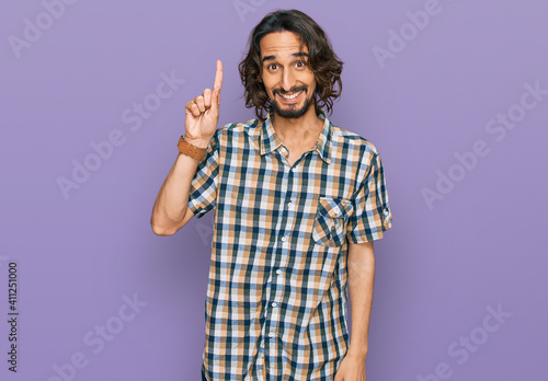 Young hispanic man wearing casual clothes pointing finger up with successful idea. exited and happy. number one.