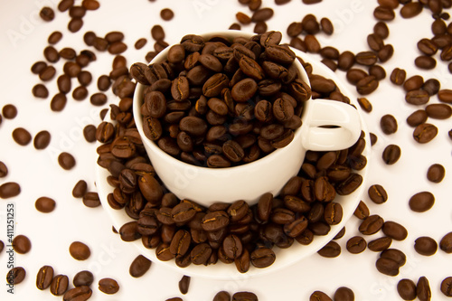 A mug with coffee surrounded by coffee beans on a white background. Coffee beans in a coffee mug