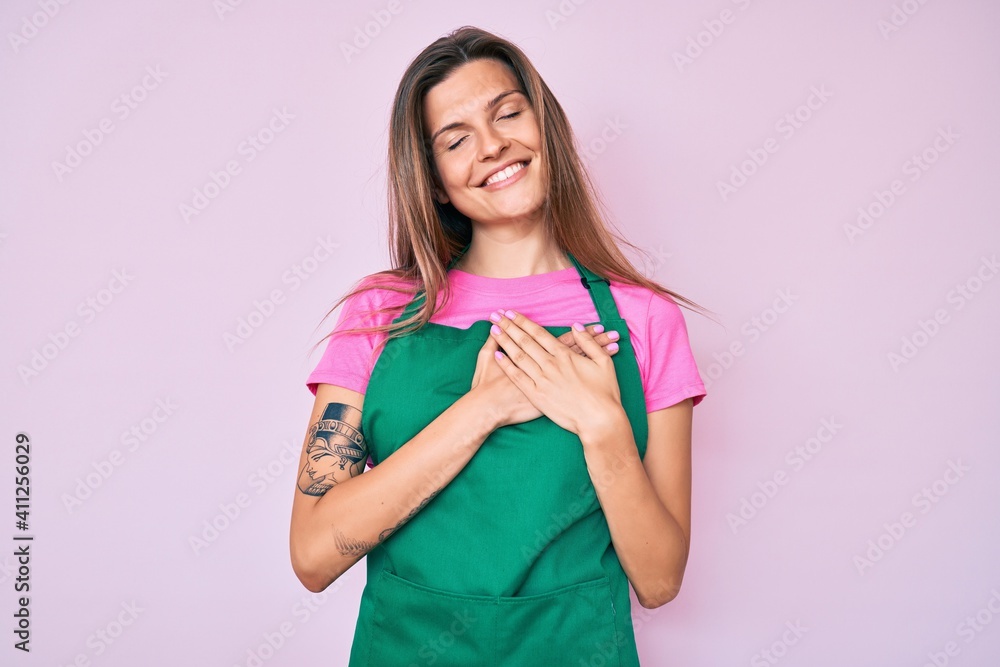 Beautiful caucasian woman wearing professional apron smiling with hands on chest with closed eyes and grateful gesture on face. health concept. Beautiful caucasian woman wearing professional apron smiling with hands on chest with closed eyes and grateful gesture on face. health concept.