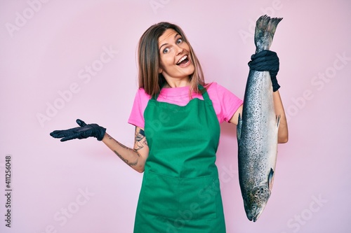 Fényképezés Beautiful caucasian woman fishmonger selling fresh raw salmon celebrating achiev