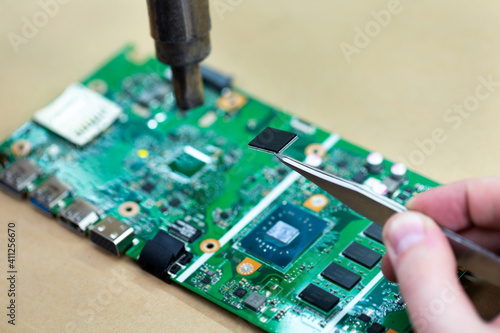 Close-up of a technician repairing a computer chip with a soldering iron, he heats the parts and disconnects them from the Board.