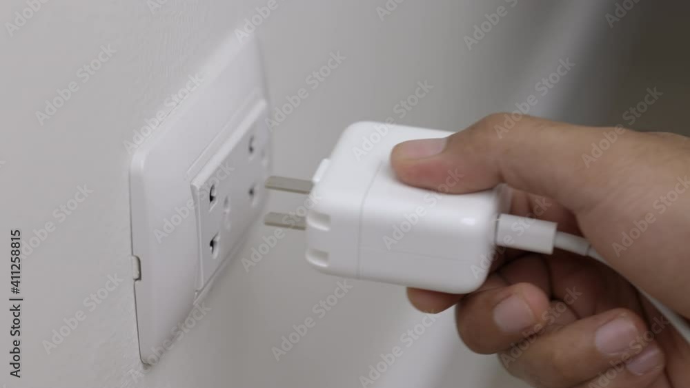 Close up male hand put on the Electric adapter smartphone or laptop plug. Electrical wires and power strips in the house Close up male hand put on the Electric adapter smartphone or laptop plug. Electrical wires and power strips in the house