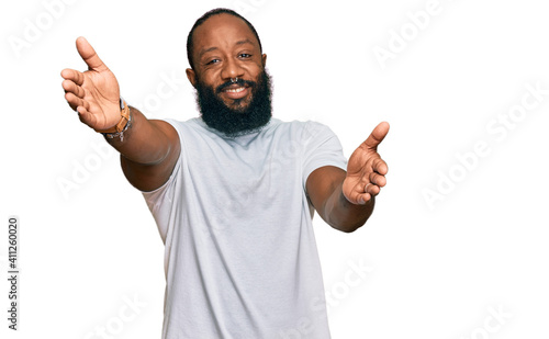 Young african american man wearing casual white tshirt looking at the camera smiling with open arms for hug. cheerful expression embracing happiness.