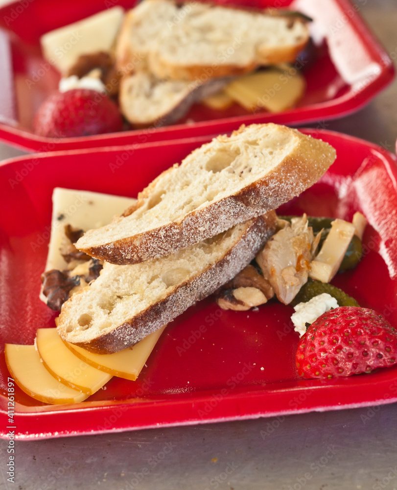 top view, close distance of a red plastic container of food samples of crusty bread, cheeses, walnuts and a strawberry, as samples at a tropical farmers market top view, close distance of a red plastic container of food samples of crusty bread, cheeses, walnuts and a strawberry, as samples at a tropical farmers market