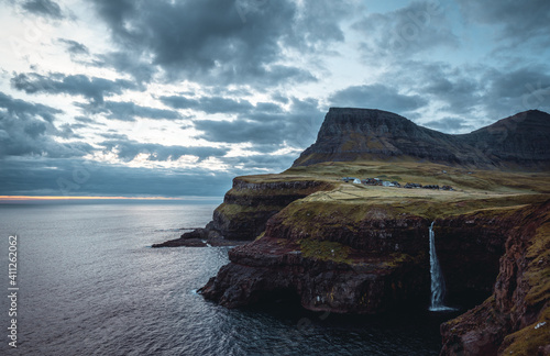 Gasadalur village and Mulafossur its iconic waterfall during sunset in summer with bluw sky. Vagar, Faroe Islands, Denmark. Rough see in the north atlantic ocean.