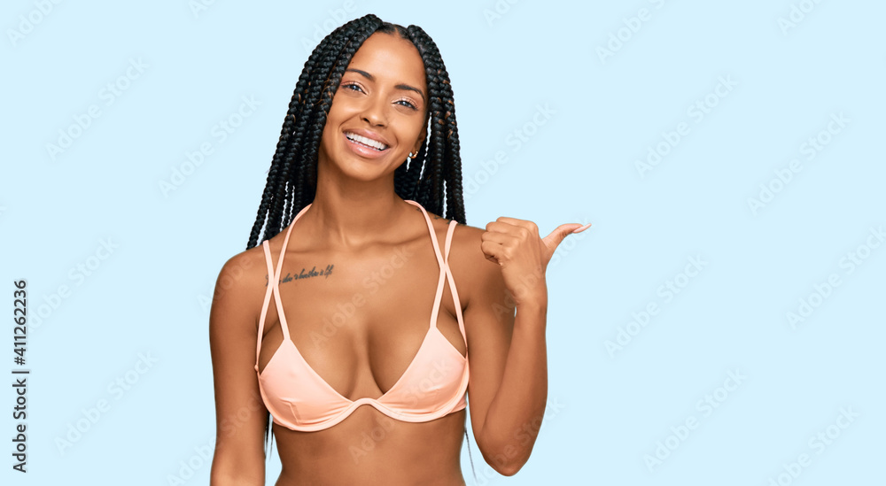 Beautiful hispanic woman wearing bikini smiling with happy face looking and pointing to the side with thumb up. Beautiful hispanic woman wearing bikini smiling with happy face looking and pointing to the side with thumb up.
