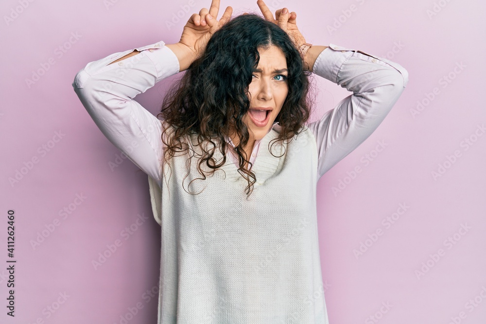 Naklejka premium Young brunette woman with curly hair wearing casual clothes posing funny and crazy with fingers on head as bunny ears, smiling cheerful