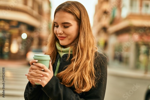 Young blonde girl smiling happy drinking coffee at the city.