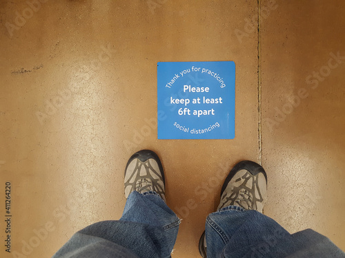 A mans feet and social distancing sign at a supermarket