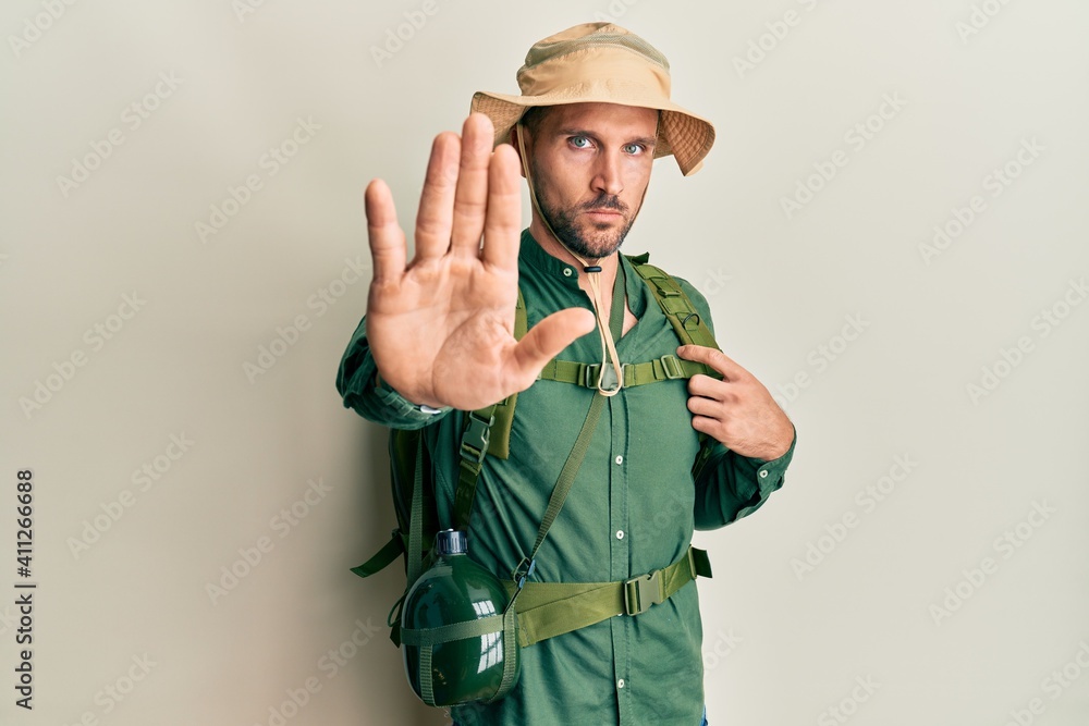 Handsome man with beard wearing explorer hat and backpack doing stop sing with palm of the hand. warning expression with negative and serious gesture on the face. Handsome man with beard wearing explorer hat and backpack doing stop sing with palm of the hand. warning expression with negative and serious gesture on the face.