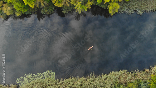 Top aerial view of the river along which a small orange kayak floats. Green trees grow on the shore. Ukraine, Europe