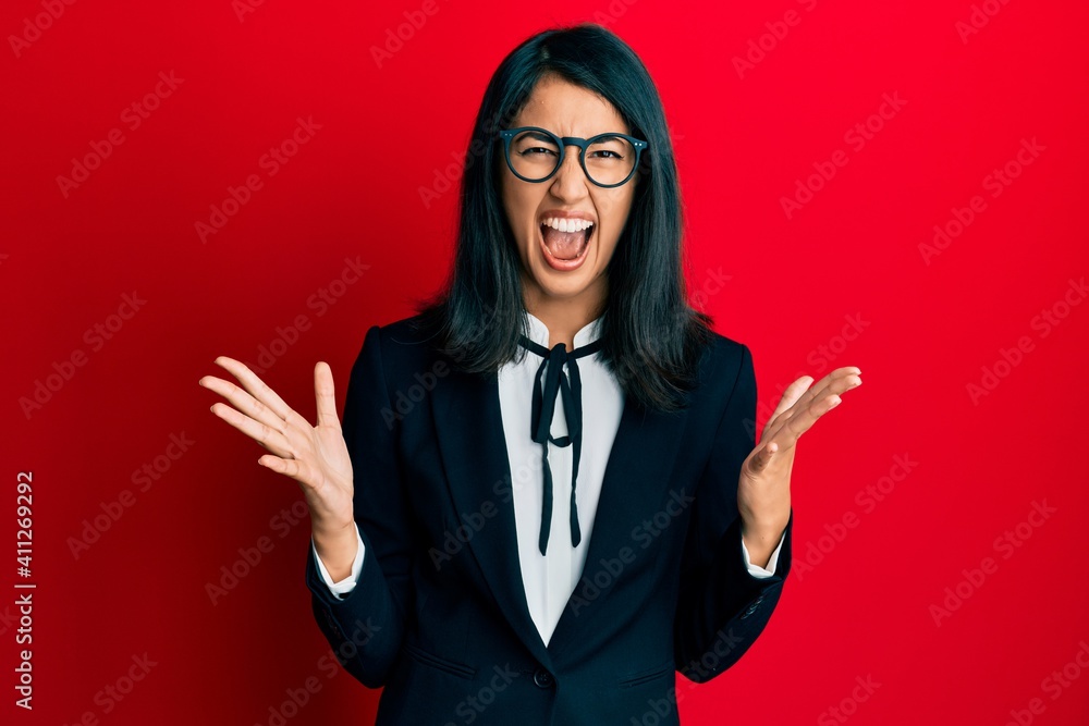 Beautiful asian young woman wearing business suit crazy and mad shouting and yelling with aggressive expression and arms raised. frustration concept. Beautiful asian young woman wearing business suit crazy and mad shouting and yelling with aggressive expression and arms raised. frustration concept.