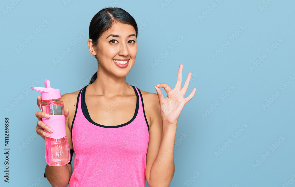 Beautiful asian young sport woman wearing sportswear drinking bottle of water doing ok sign with fingers, smiling friendly gesturing excellent symbol Beautiful asian young sport woman wearing sportswear drinking bottle of water doing ok sign with fingers, smiling friendly gesturing excellent symbol