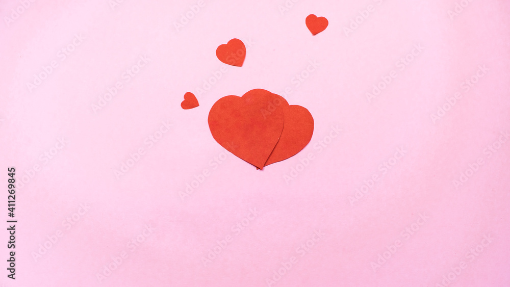 Two big red and three small hearts as symbol of love isolated on light pink background.