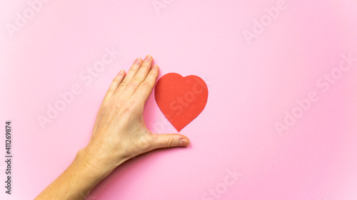 Heart between the fingers of a woman's hand isolated on light pink background