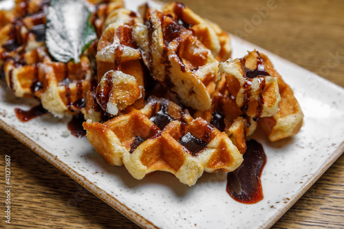 Freshly baked shortbread waffles, drizzled with chocolate, decorated with basil leaves, served on a rectangular plate on a wooden background. Dessert at the restaurant.