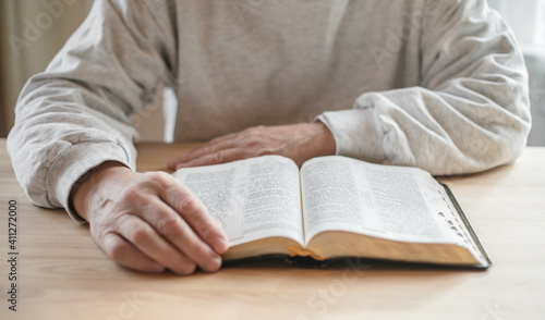 senior man praying, reading  an old Bible in his hands.