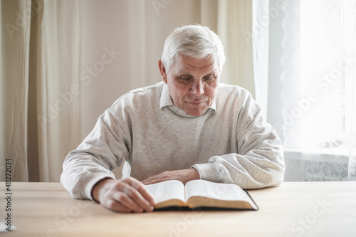 senior man praying, reading an old Bible in his hands.