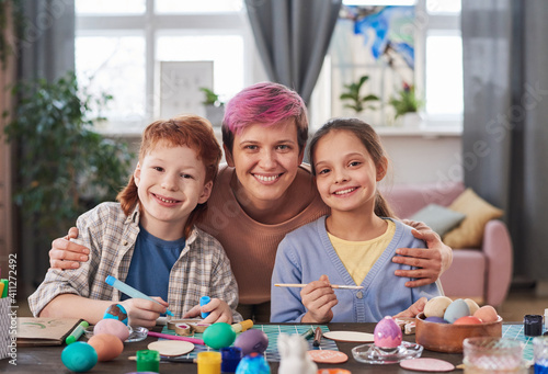 Portrait of happy mother with her two children smiling at camera while decorating and painting eggs for Easter