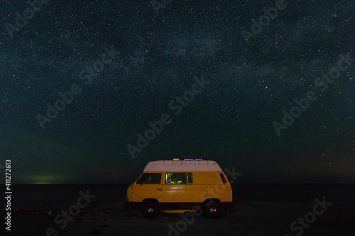 Yellow vintage camper van at night parking under the starry sky.