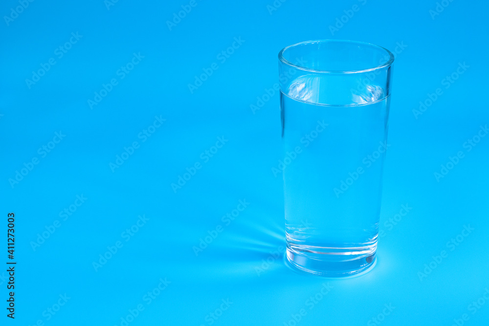 A glass of water on a blue background. The sun's rays are reflected in the water and on the background. A glass of water on a blue background. The sun's rays are reflected in the water and on the background.
