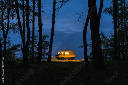 Yellow vintage camper van parked in the forest at night. Camping in the wild nature.