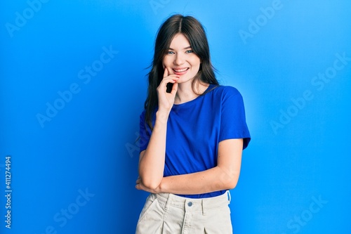 Young beautiful caucasian girl wearing casual clothes smiling looking confident at the camera with crossed arms and hand on chin. thinking positive.