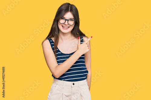Young beautiful caucasian girl wearing casual clothes and glasses cheerful with a smile of face pointing with hand and finger up to the side with happy and natural expression on face