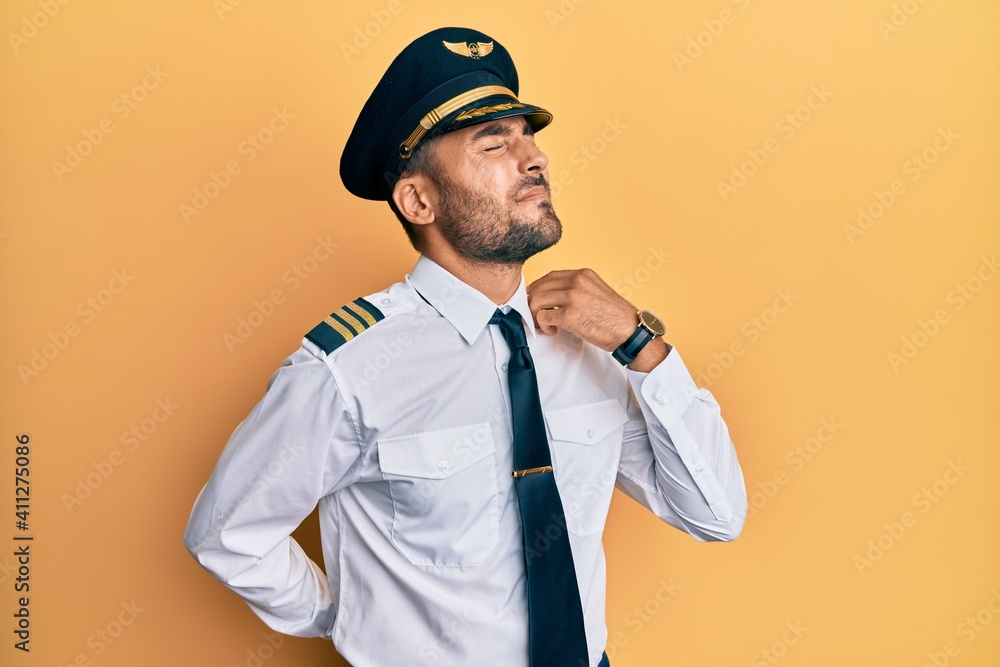 Handsome hispanic man wearing airplane pilot uniform suffering of neck ache injury, touching neck with hand, muscular pain Handsome hispanic man wearing airplane pilot uniform suffering of neck ache injury, touching neck with hand, muscular pain