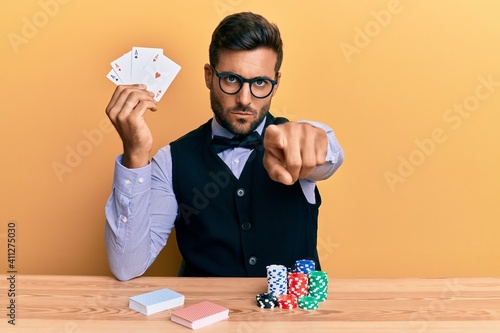 Photos Handsome hispanic croupier man sitting on the table with poker chips and cards p