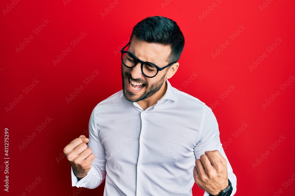 Young hispanic businessman wearing shirt and glasses excited for success with arms raised and eyes closed celebrating victory smiling. winner concept. Young hispanic businessman wearing shirt and glasses excited for success with arms raised and eyes closed celebrating victory smiling. winner concept.