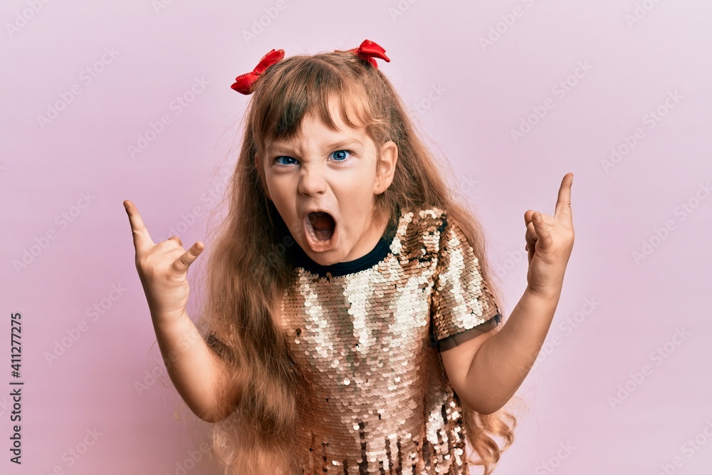 Little caucasian girl kid wearing festive sequins dress shouting with crazy expression doing rock symbol with hands up. music star. heavy concept. - obrazy, fototapety, plakaty 